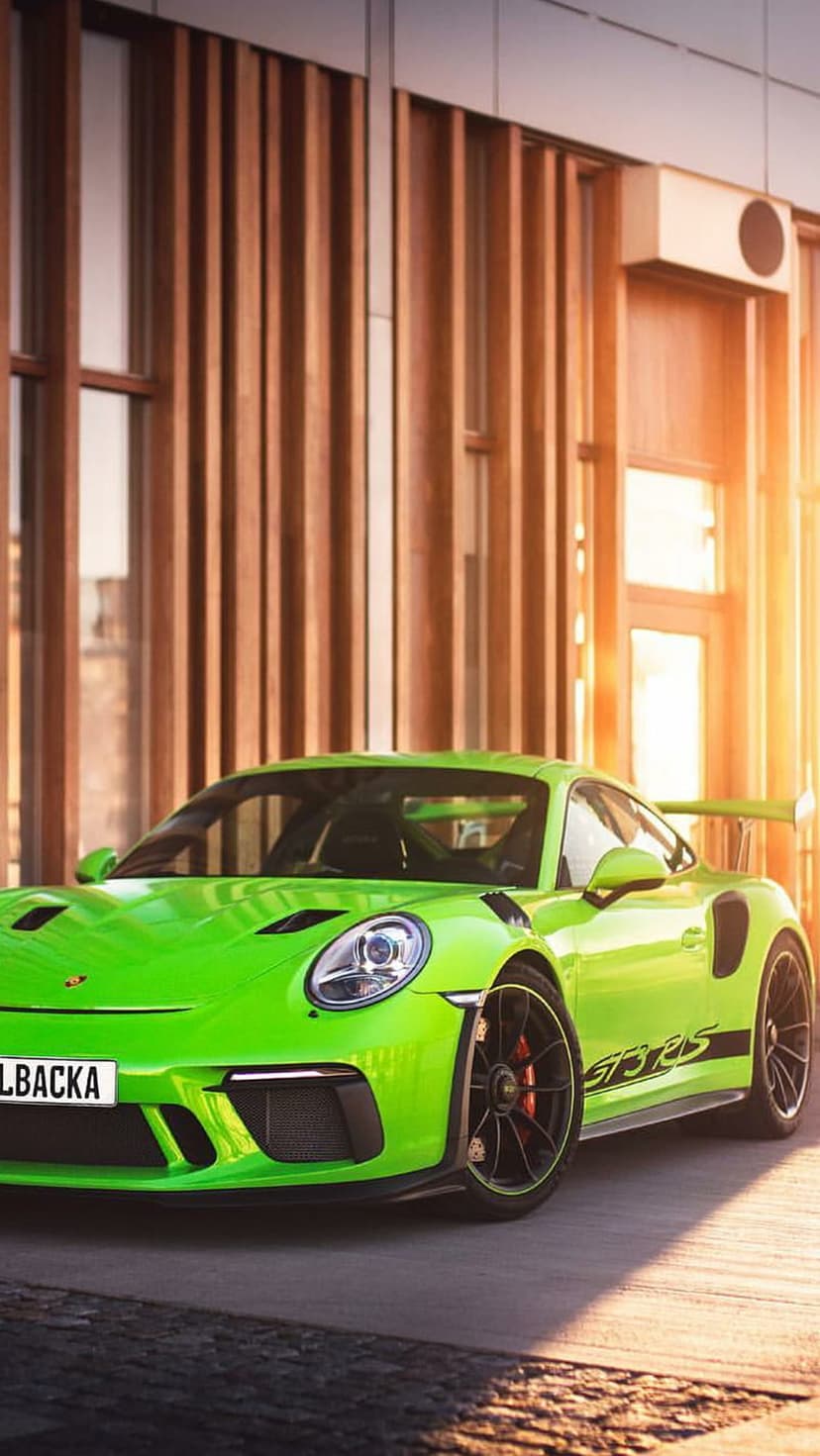 Lime green Porsche GT3 RS parked beside a slatted wood building at sunset, showing the sleek car profile and rims.