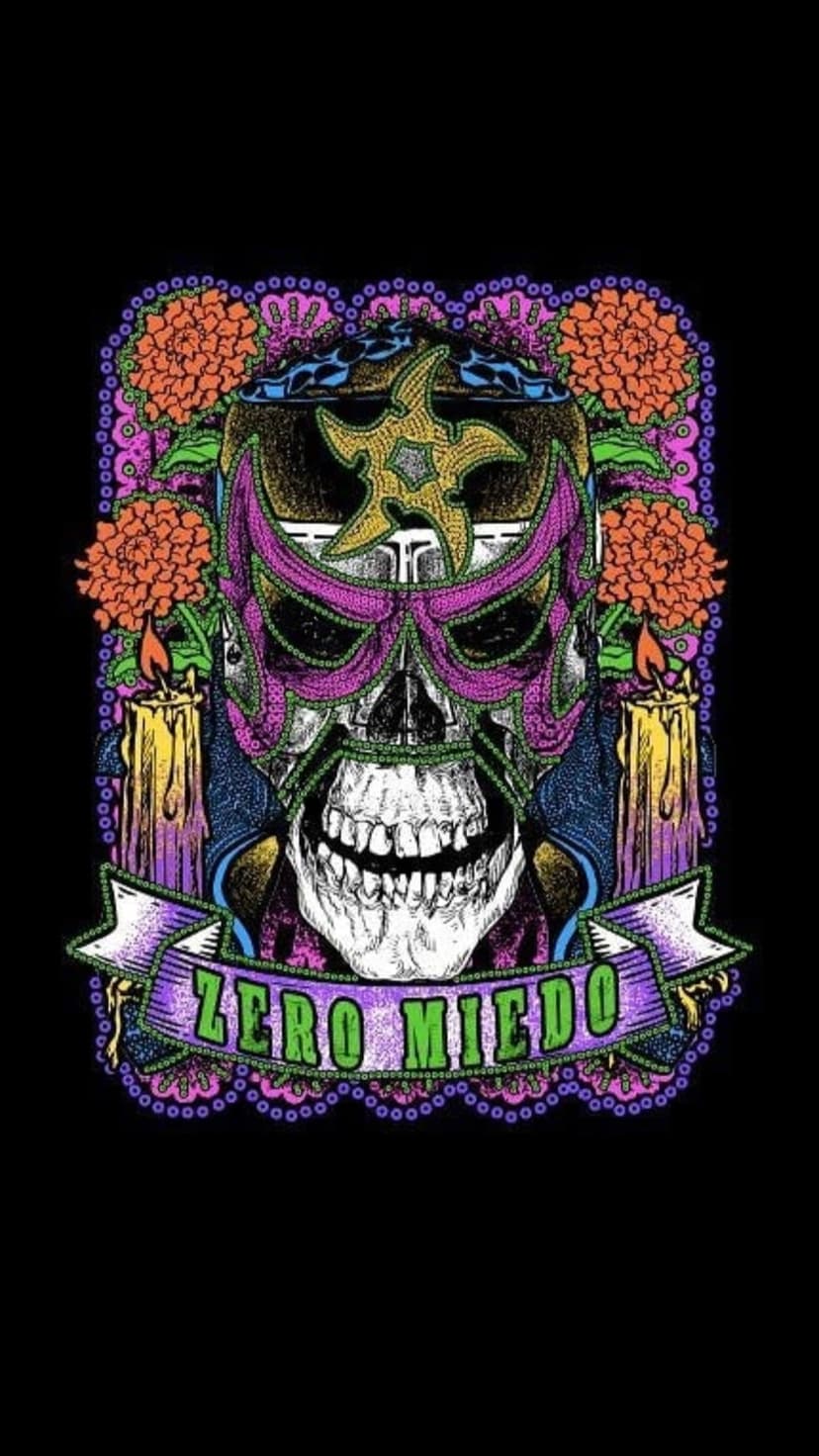 Skull wearing a decorative lucha libre mask surrounded by orange marigolds and flickering ritual candles.