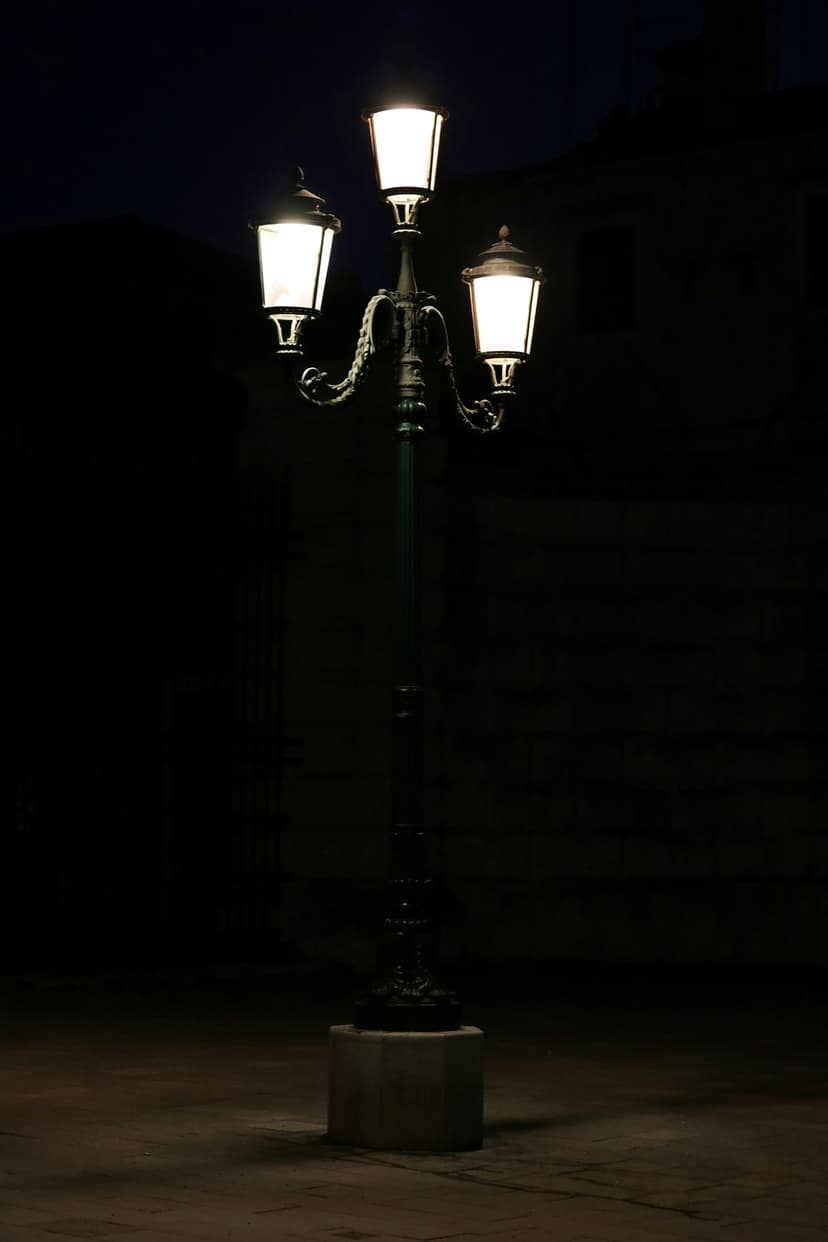 Ornate three-lamp street light with glowing hexagonal lanterns against a dark night sky on a paved city street.