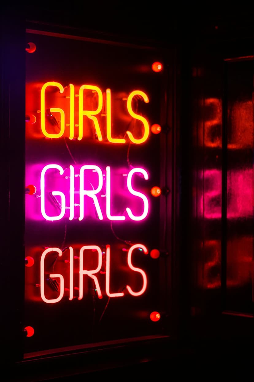 Three stacked neon signs displaying the word Girls in orange, pink, and red hues against a dark glass surface.