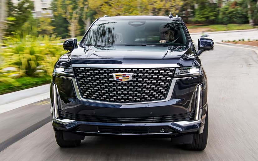 Front view of a dark blue Cadillac Escalade driving on a road with motion blur and a large chrome grille.