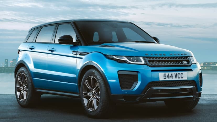 Blue Range Rover Evoque luxury SUV parked on asphalt against a soft cloudy sky background in landscape.