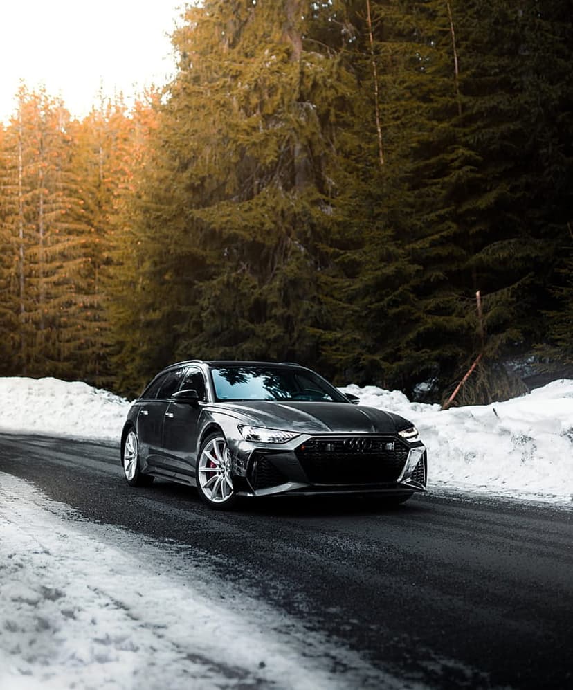 Audi RS6 Avant drives on a wet snowy road through sunlit pine trees in a vertical winter car wallpaper.