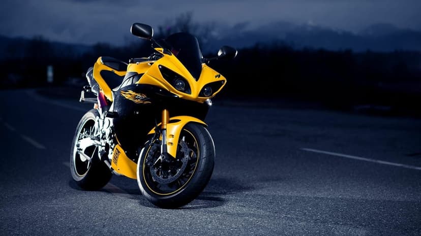 Yellow Yamaha motorcycle with dual headlights on a dark asphalt road at dusk against a mountain backdrop.