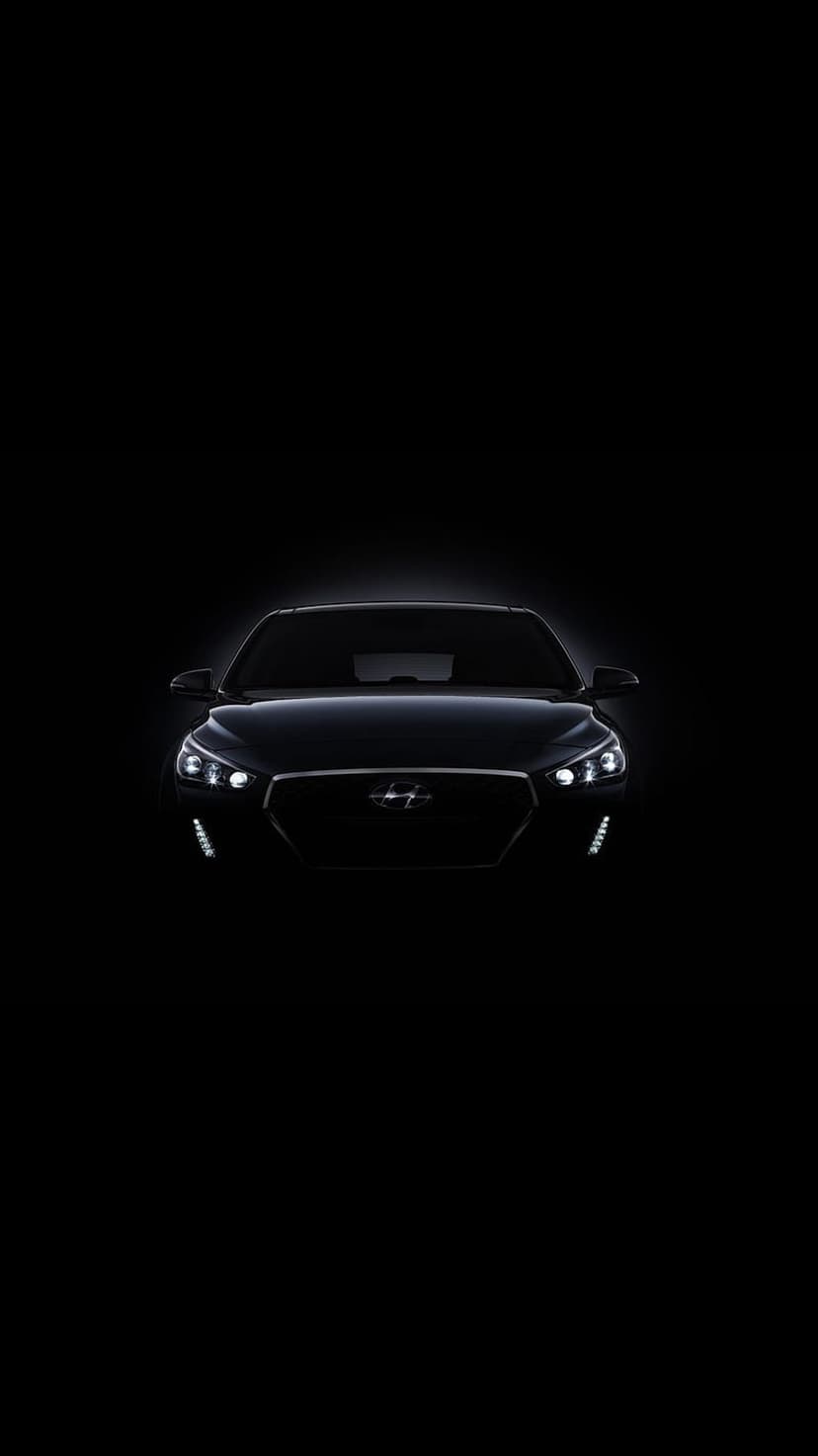 Hyundai i30 front view with glowing LED headlights and a mesh grille visible against a pitch black background.
