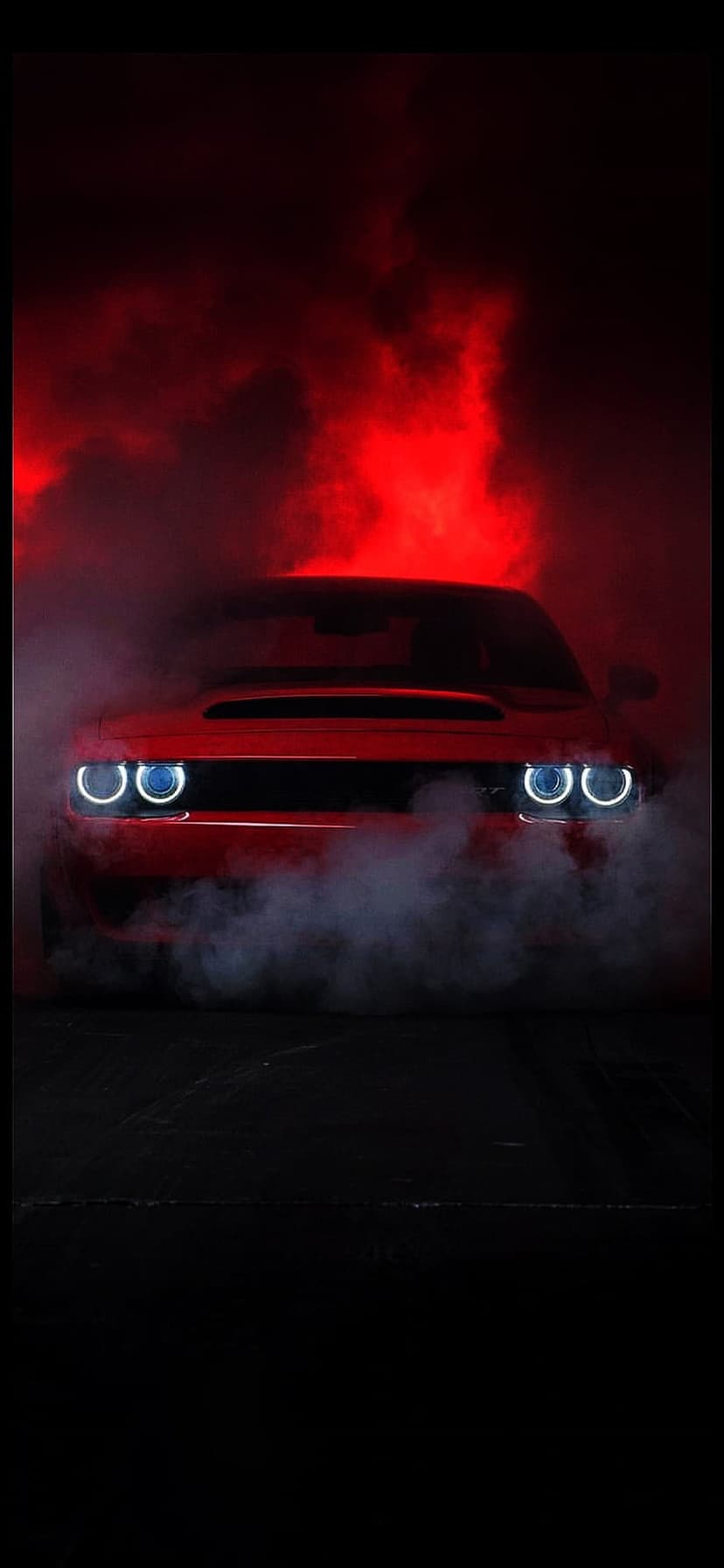 Red Dodge Challenger with glowing circular headlights emerging from thick white smoke under intense red lighting.