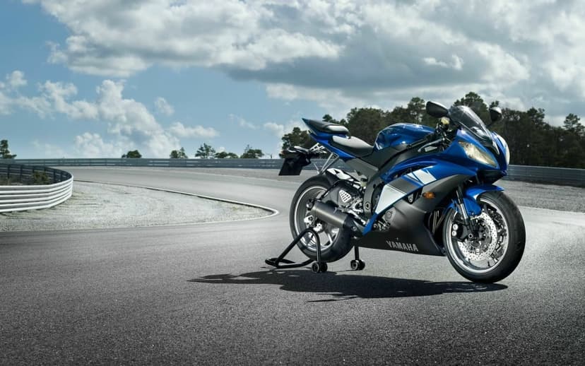 Blue Yamaha YZF-R6 motorcycle on a rear stand on a curved asphalt race track under a bright cloudy sky.