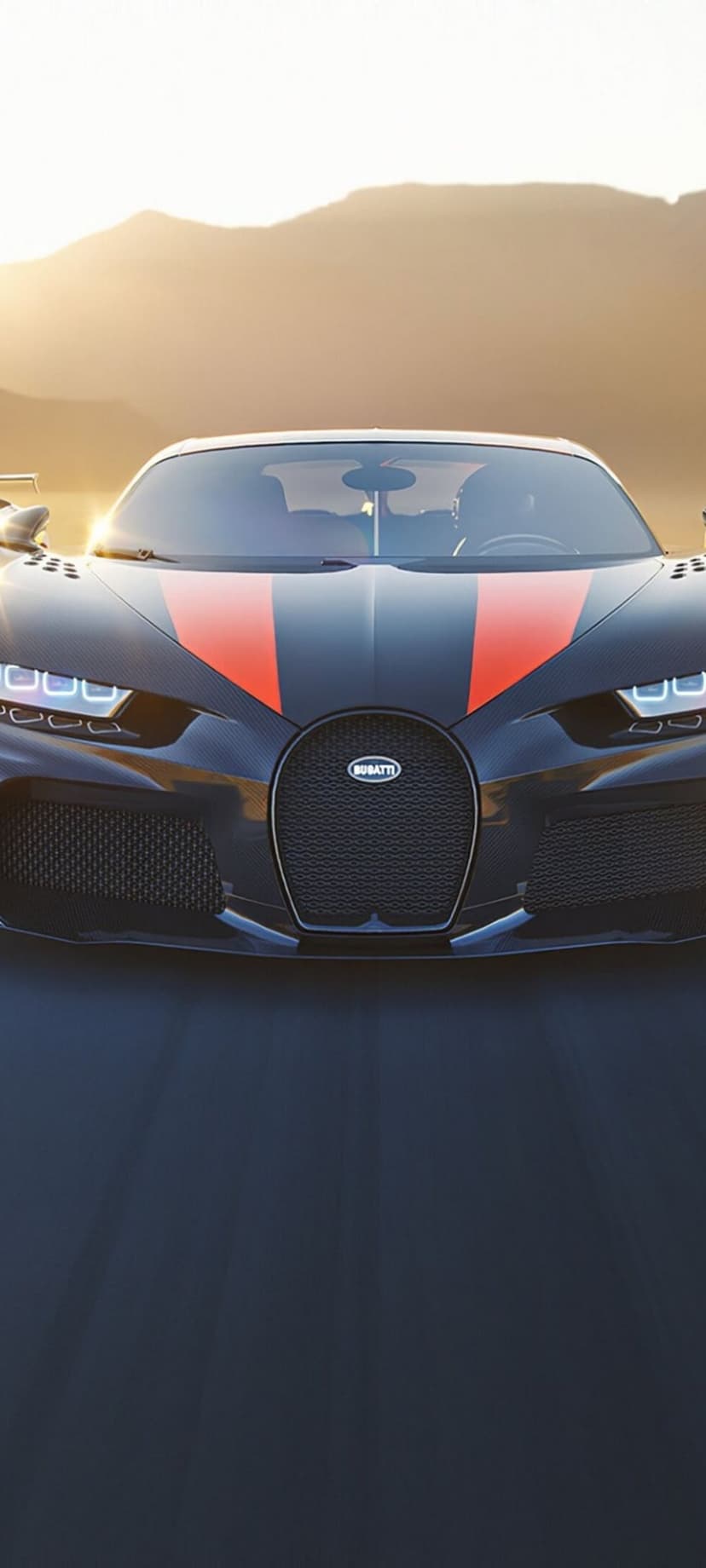 Bugatti Chiron Sport with orange stripes drives on a mountain road during a golden sunset with glowing headlights.