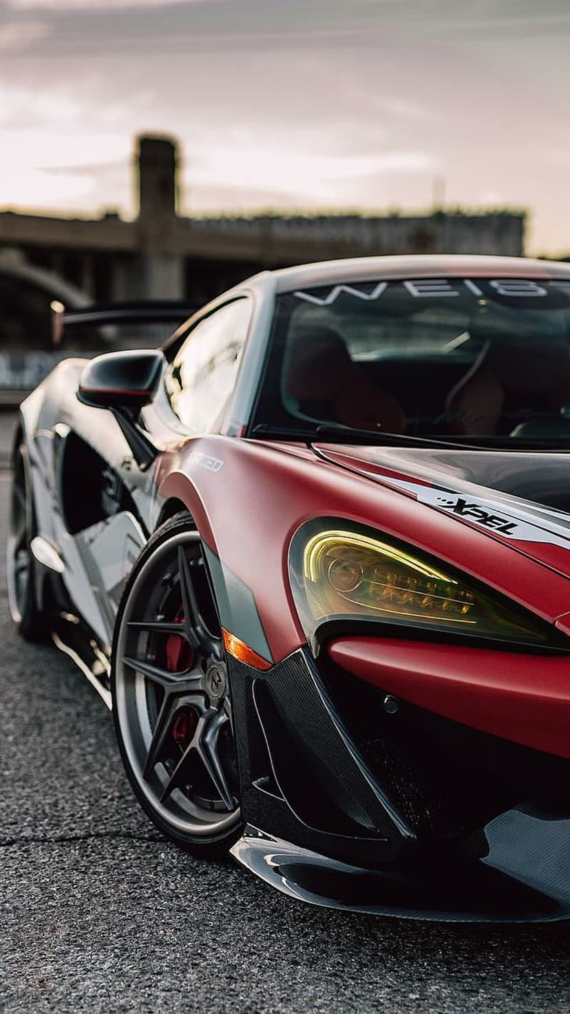 McLaren 720S Spyder with red and white racing livery parked on asphalt against a blurred industrial backdrop.