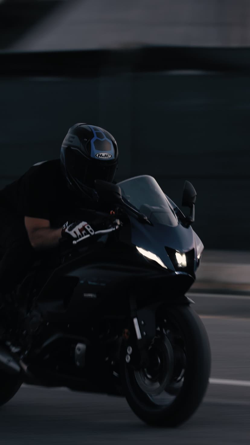 Motorcyclist in black gear riding a sportbike with glowing headlights on a blurred asphalt road at dusk.