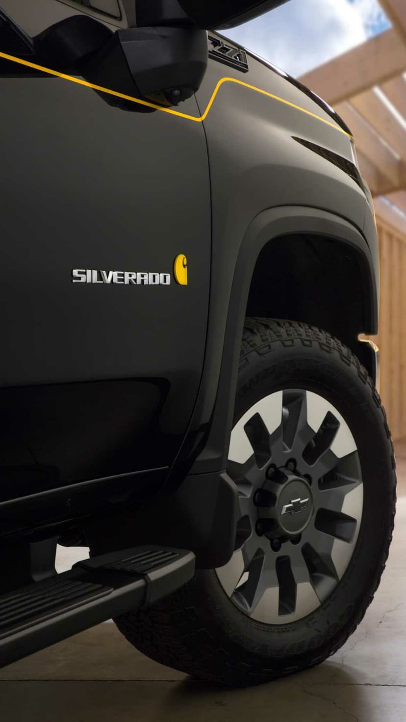 Matte black Chevrolet Silverado truck with Carhartt logo, yellow pinstripe, and rugged off-road wheels.