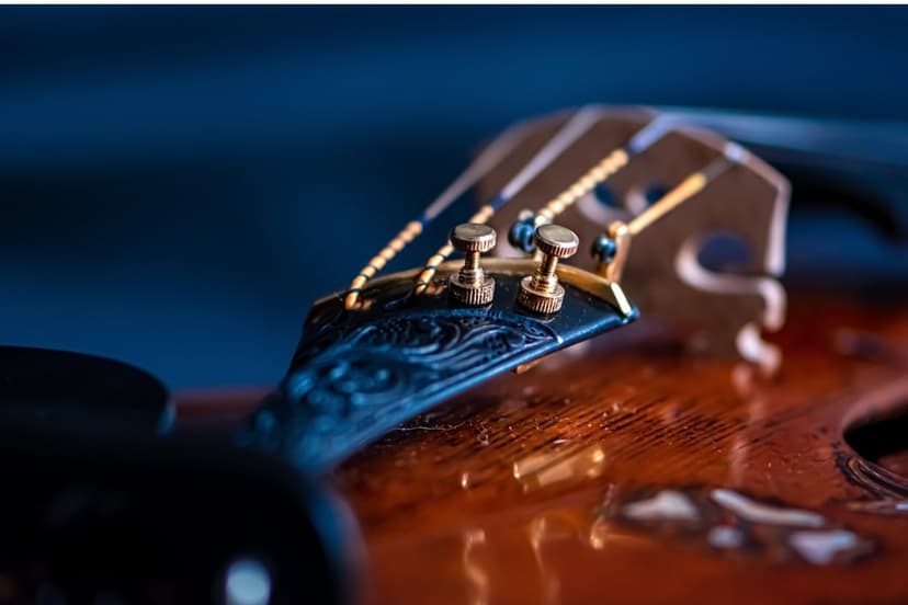 Hand-carved ebony violin scroll featuring gold-plated tuning pegs against a deep blue atmospheric background.