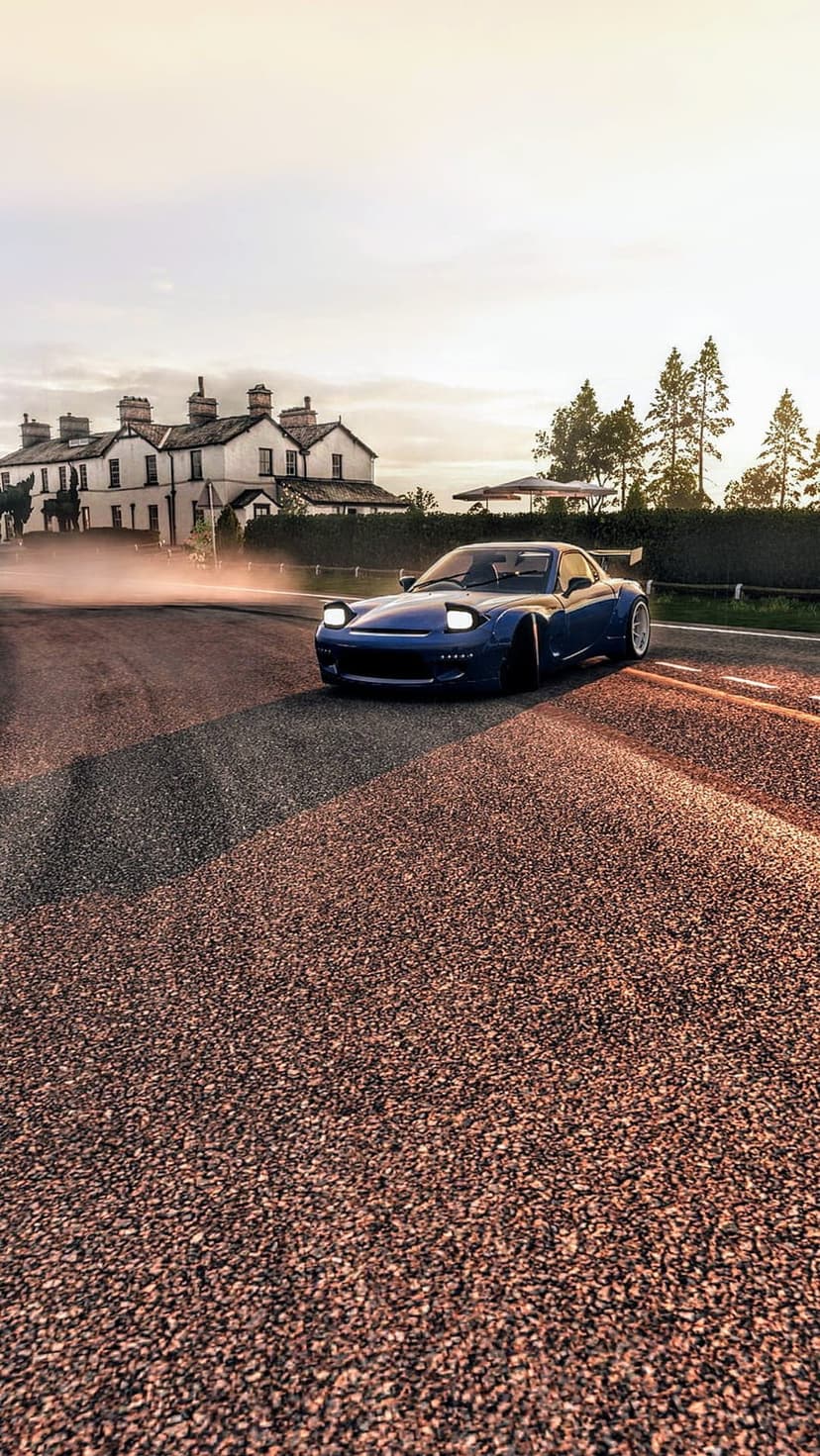 Blue sports car drifting on a gravel road at sunset with dust clouds near a white rural farmhouse.