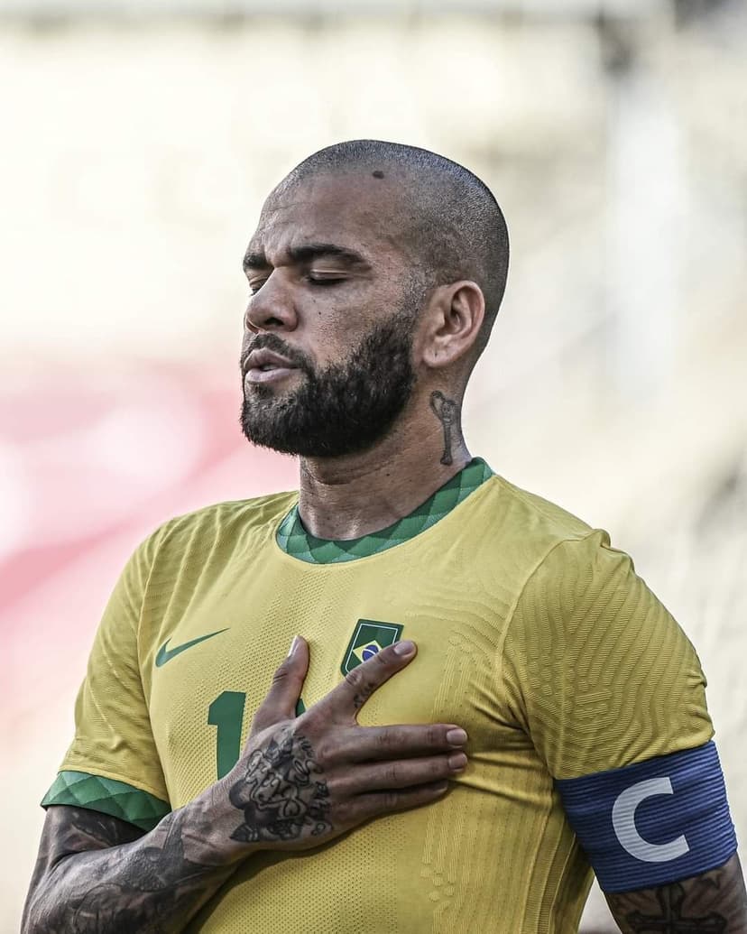 Dani Alves with eyes closed and hand on heart wearing a yellow Brazil jersey and captain's armband.