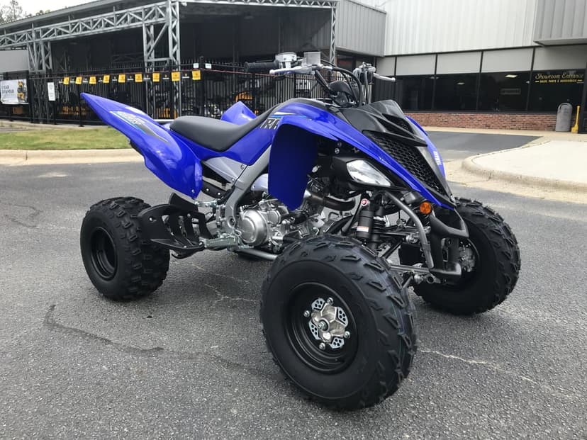 Blue Yamaha Raptor 700R ATV parked on asphalt with black knobby tires and silver engine details.