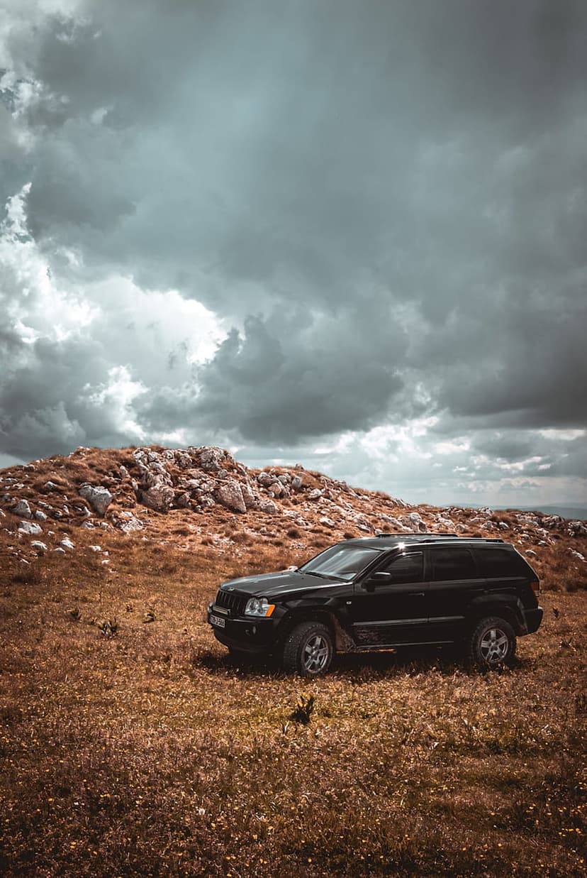Black Jeep Grand Cherokee parked on a rocky, dry hillside under a dark, dramatic overcast sky with heavy clouds.