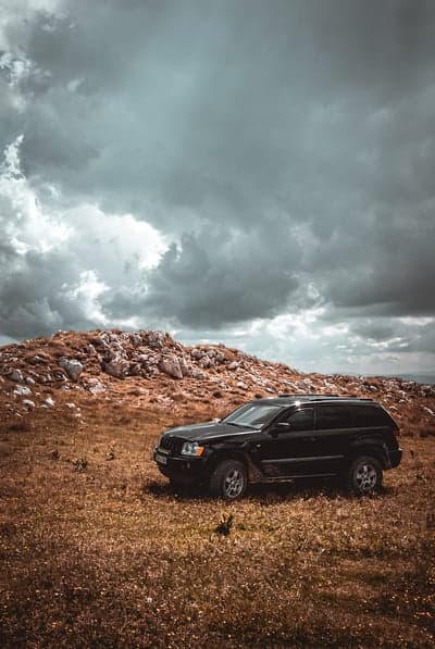 Black Jeep on a rocky hill under stormy clouds