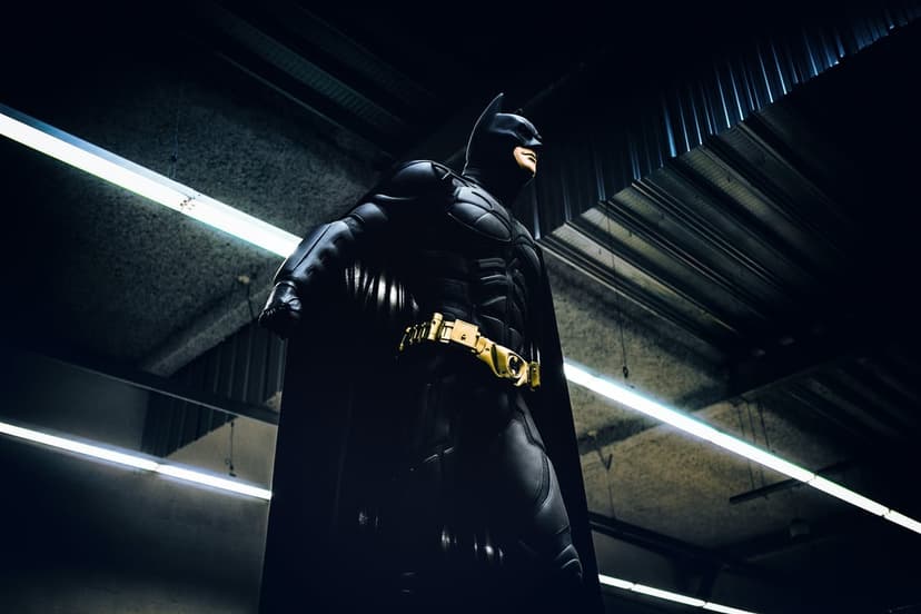 Batman statue in black and gold armor stands under fluorescent ceiling lights with deep industrial shadows.