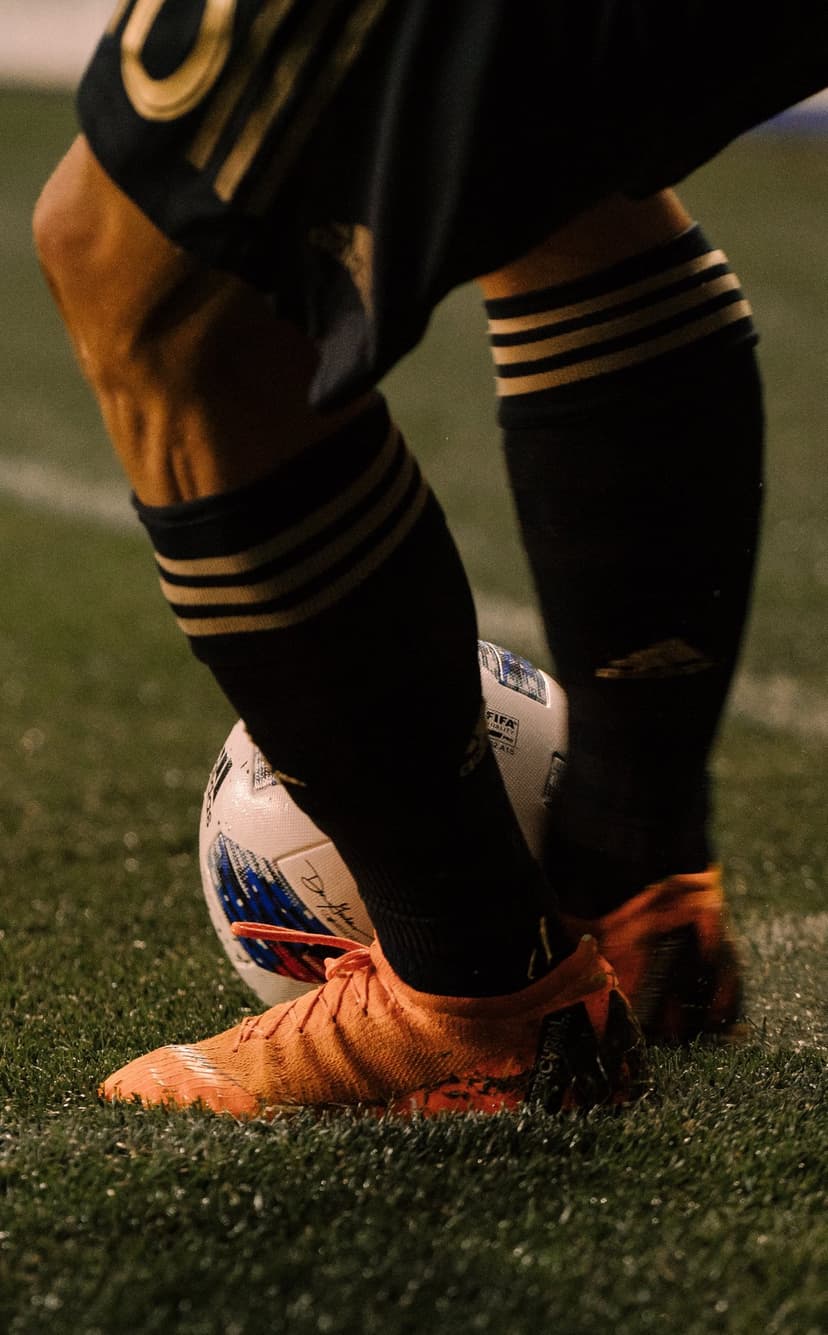 Soccer player's legs in orange cleats and black socks control a ball on green grass under twilight lighting.