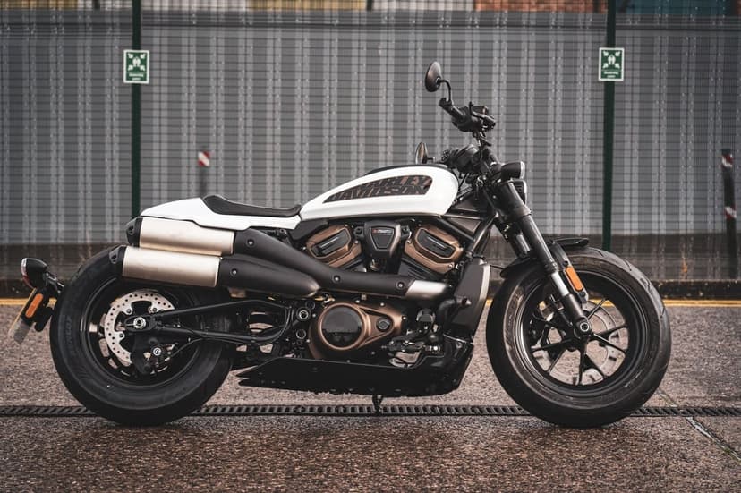 White Harley-Davidson Sportster S motorcycle side profile on wet pavement against a grey industrial fence.