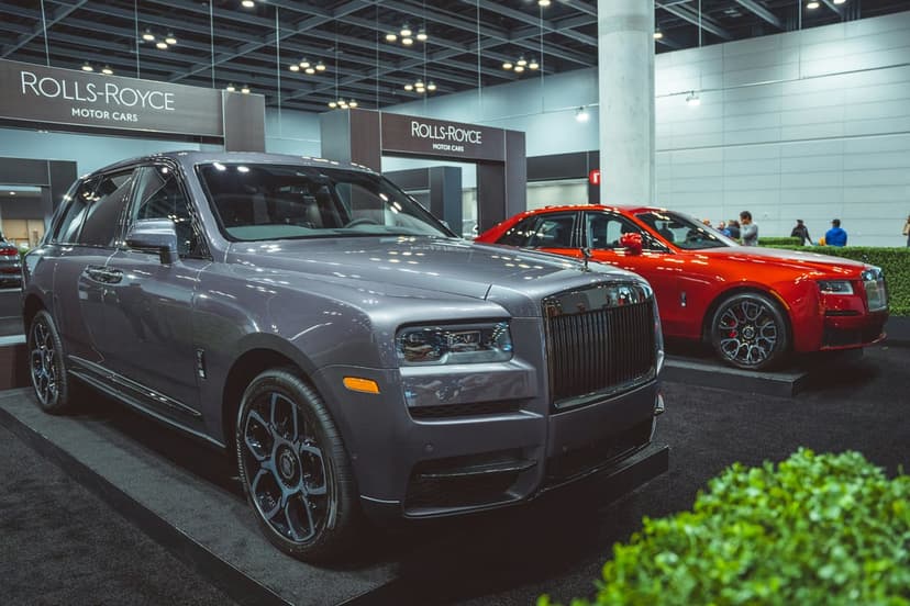 Grey Rolls-Royce Cullinan SUV and red Wraith coupe parked on dark platforms at a luxury automotive exhibition.