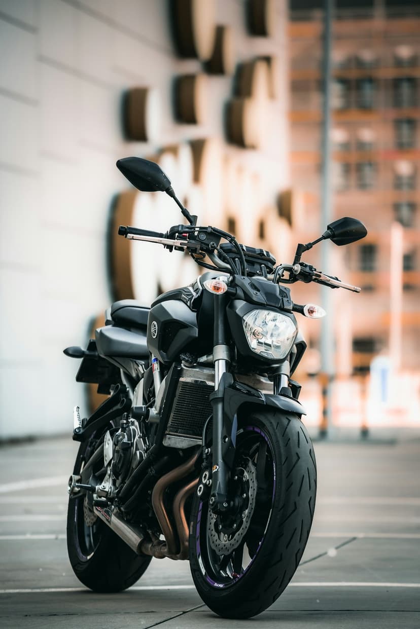 Matte black motorcycle with visible headlights and front tire parked in front of a modern stone building.