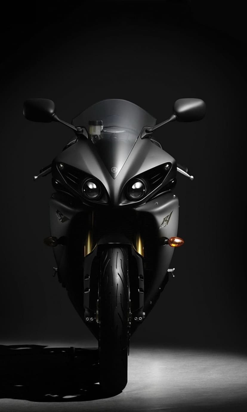Yamaha R1 sportbike front view featuring matte black fairings and illuminated dual headlights on a dark background.