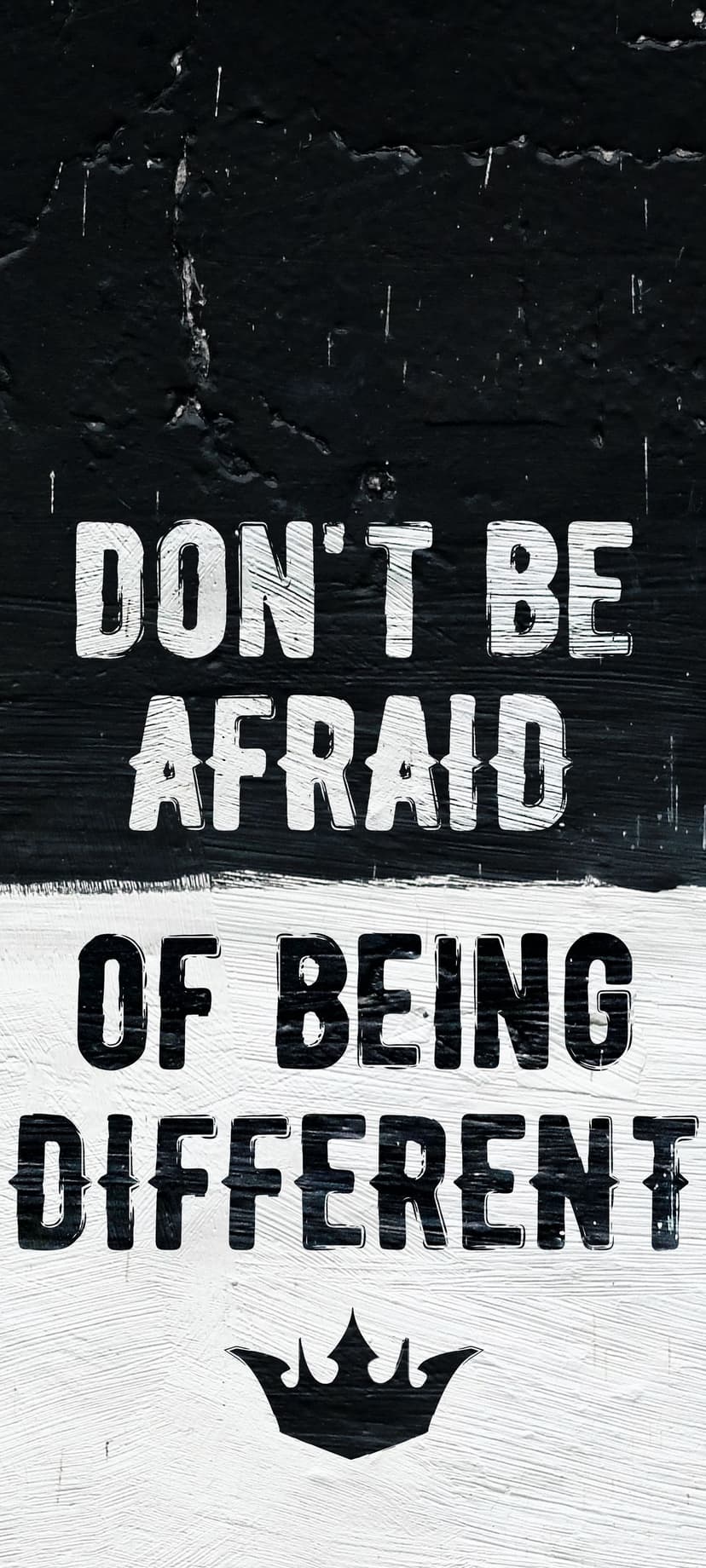 Motivational quote text Don't Be Afraid Of Being Different with a small crown on a dark textured background.