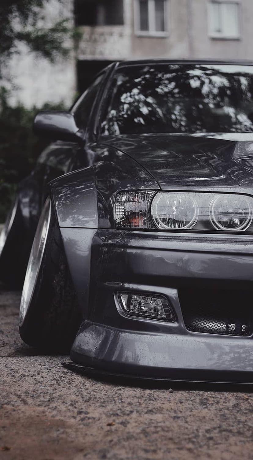 Nissan Silvia S15 widebody car with a slammed stance parked on dark asphalt under soft urban lighting.