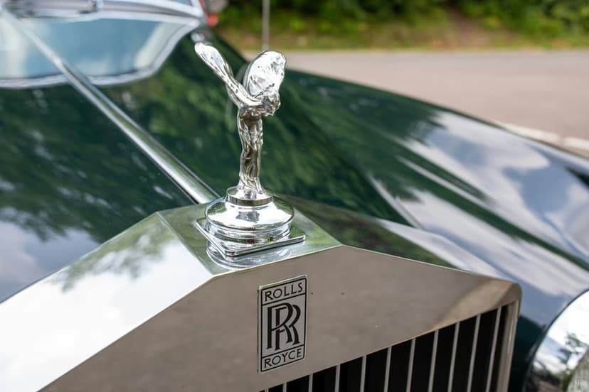 Spirit of Ecstasy figurine and RR badge on a chrome grille against the dark green paint of a vintage car.