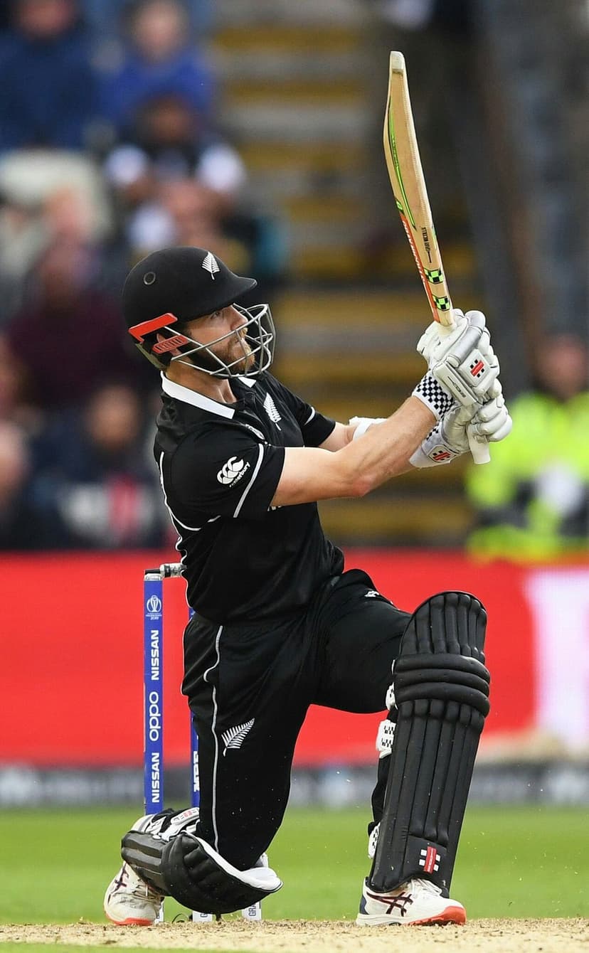 Kane Williamson batting in black cricket gear with visible stumps and blurred stadium floodlights in background.