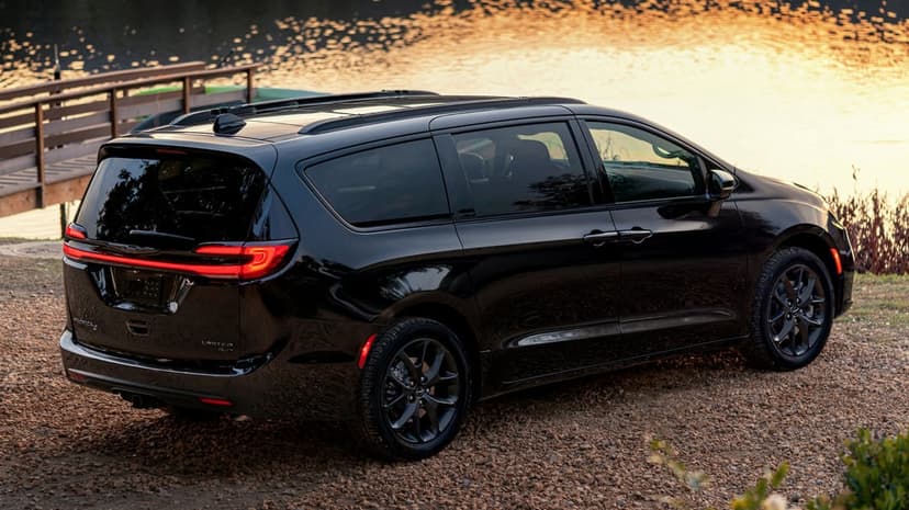 Rear view of a black Chrysler Pacifica parked on gravel near a calm lake during golden hour sunset.