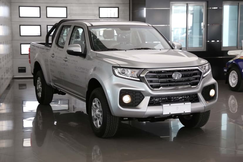 Silver pickup truck with glowing fog lights on a reflective studio floor in a modern showroom.