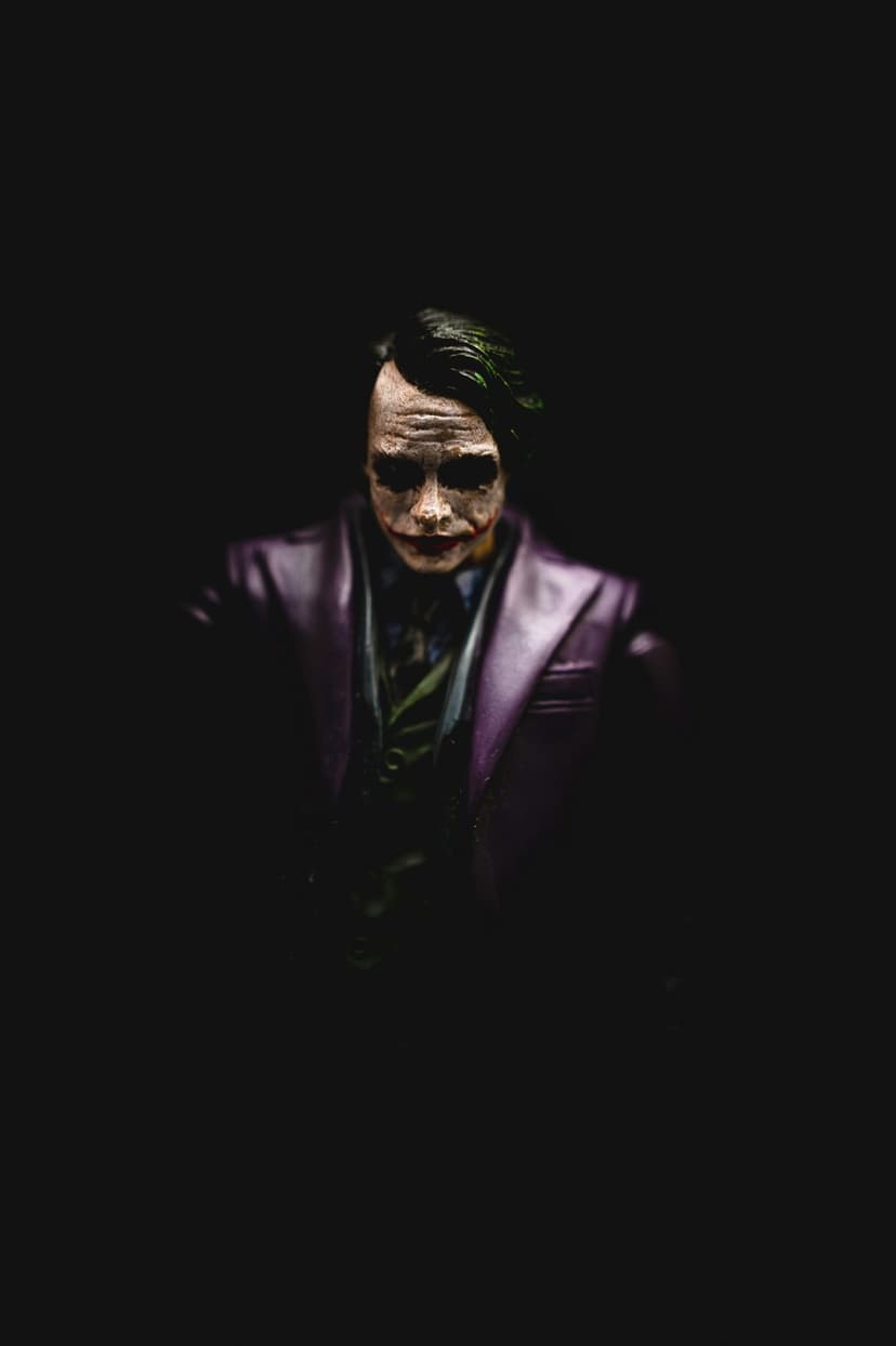 Joker figurine with green hair and purple suit stares intensely from a dark and heavily shadowed background.