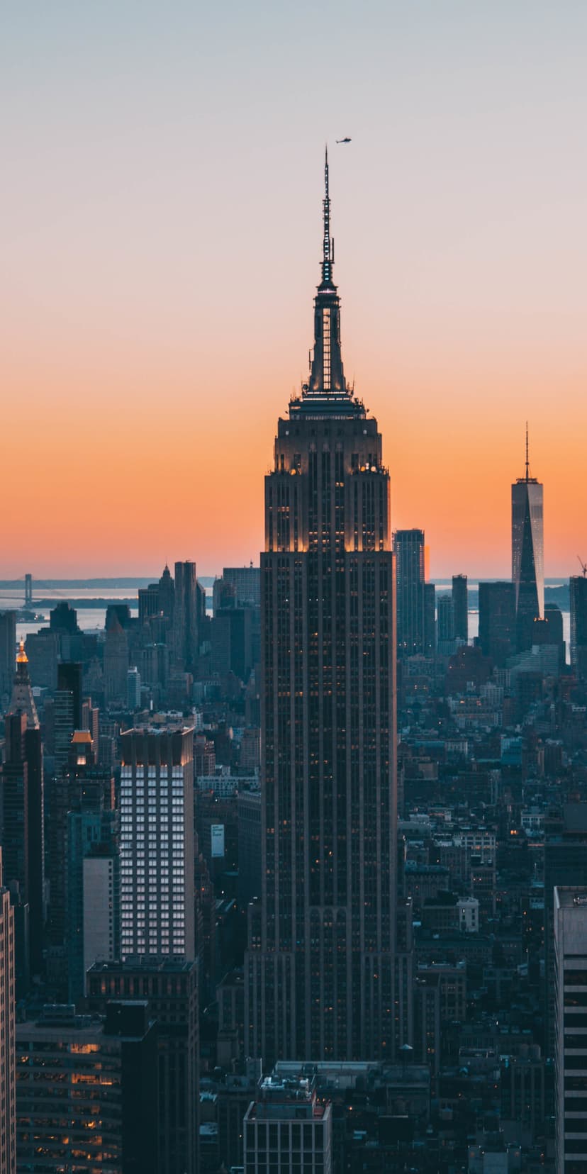 Empire State Building glows with golden sunset light against a sprawling New York City skyline at dusk.