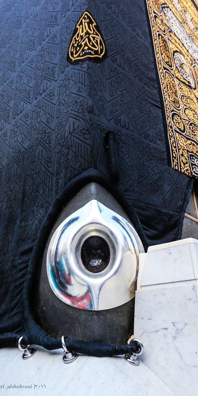 Hajar al-Aswad in a silver frame against black Kiswah fabric with golden Arabic calligraphy in Mecca.