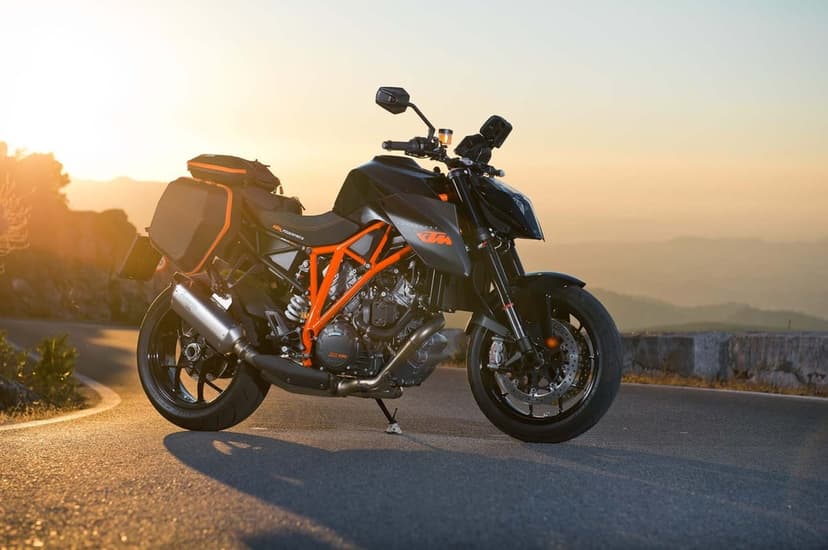 KTM 1290 Super Duke R with touring bags on a mountain road during a warm sunset with hazy hills.