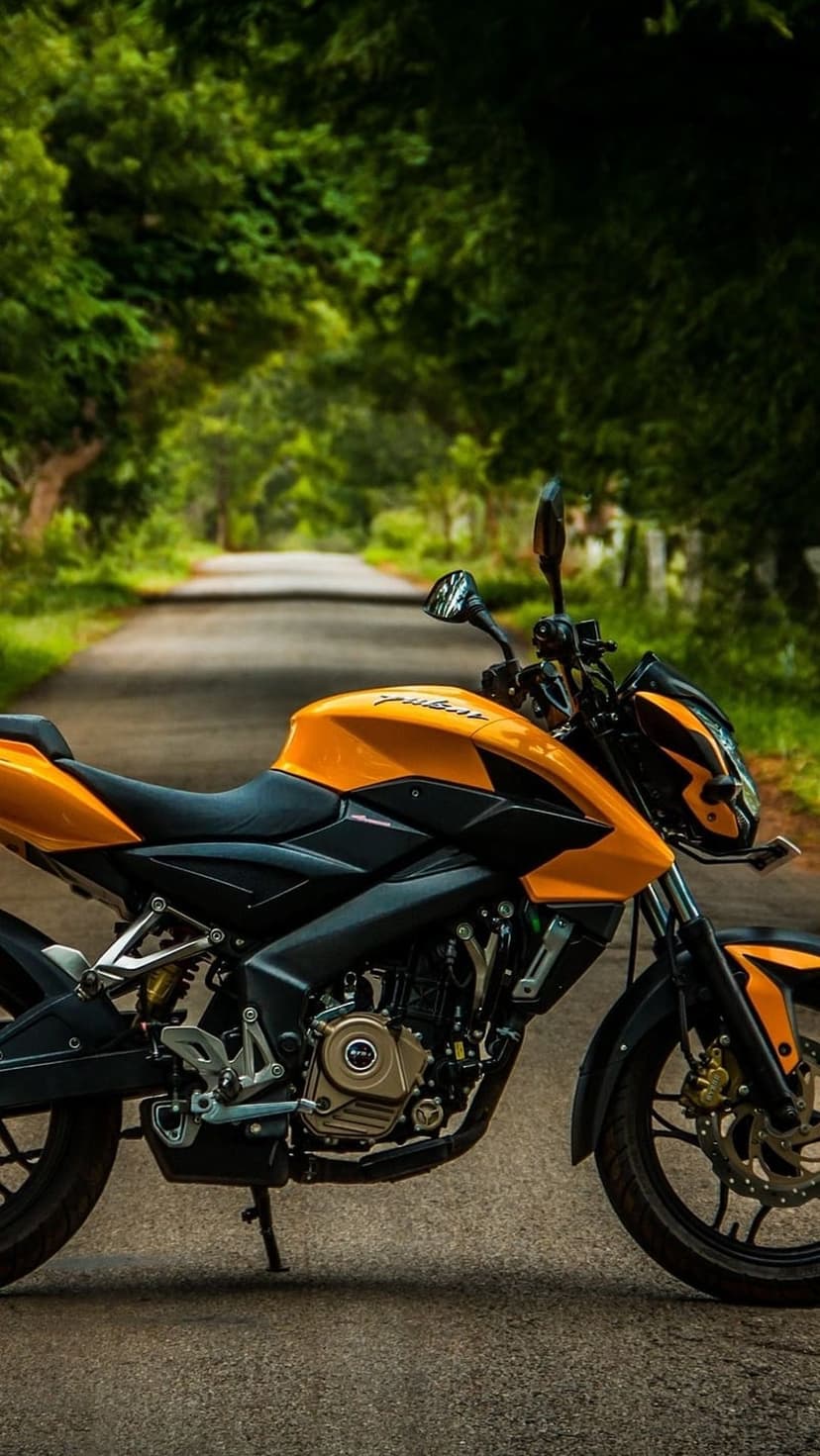 Orange and black sport motorcycle parked on a grey asphalt road with lush green trees in the background.
