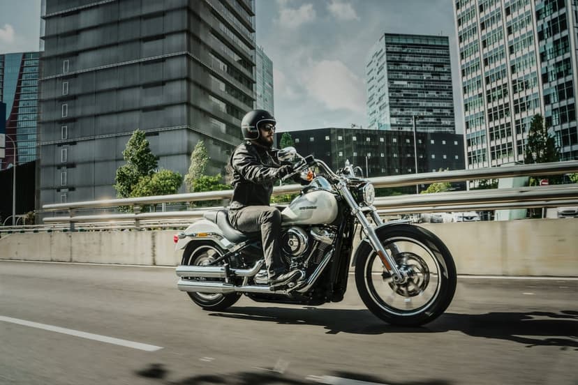 Motorcyclist in leather riding a white cruiser past glass skyscrapers with motion blur on a city street.