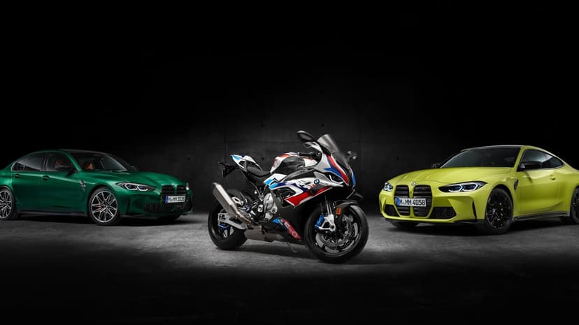 Green BMW M3 sedan and yellow M4 coupe flanking an M 1000 RR motorcycle in a dark industrial studio.