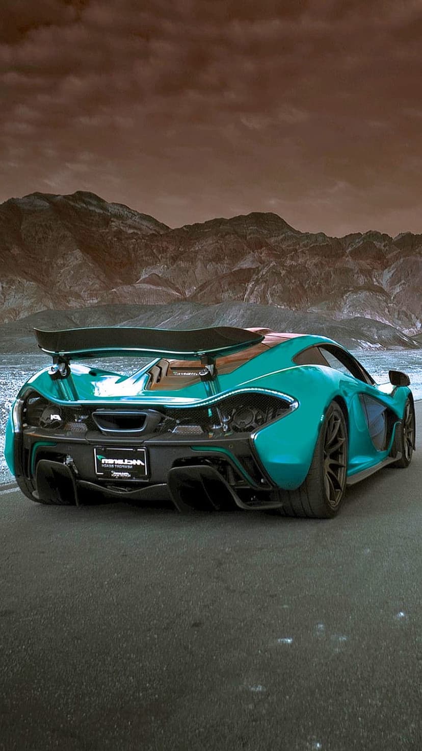 Teal McLaren P1 hypercar rear view speeding on a desert road with rugged mountains under a cloudy sky.