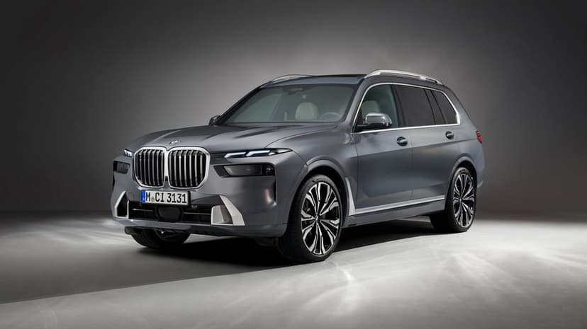 Gray BMW X7 luxury SUV in a studio with bright headlights, chrome grille, and large multi-spoke wheels.