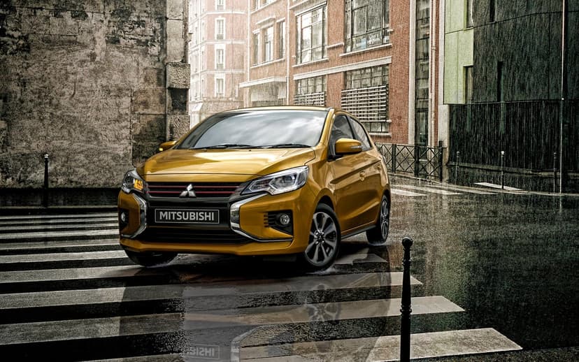 Yellow Mitsubishi Mirage parked on a wet crosswalk in an urban street with brick buildings and soft lighting.