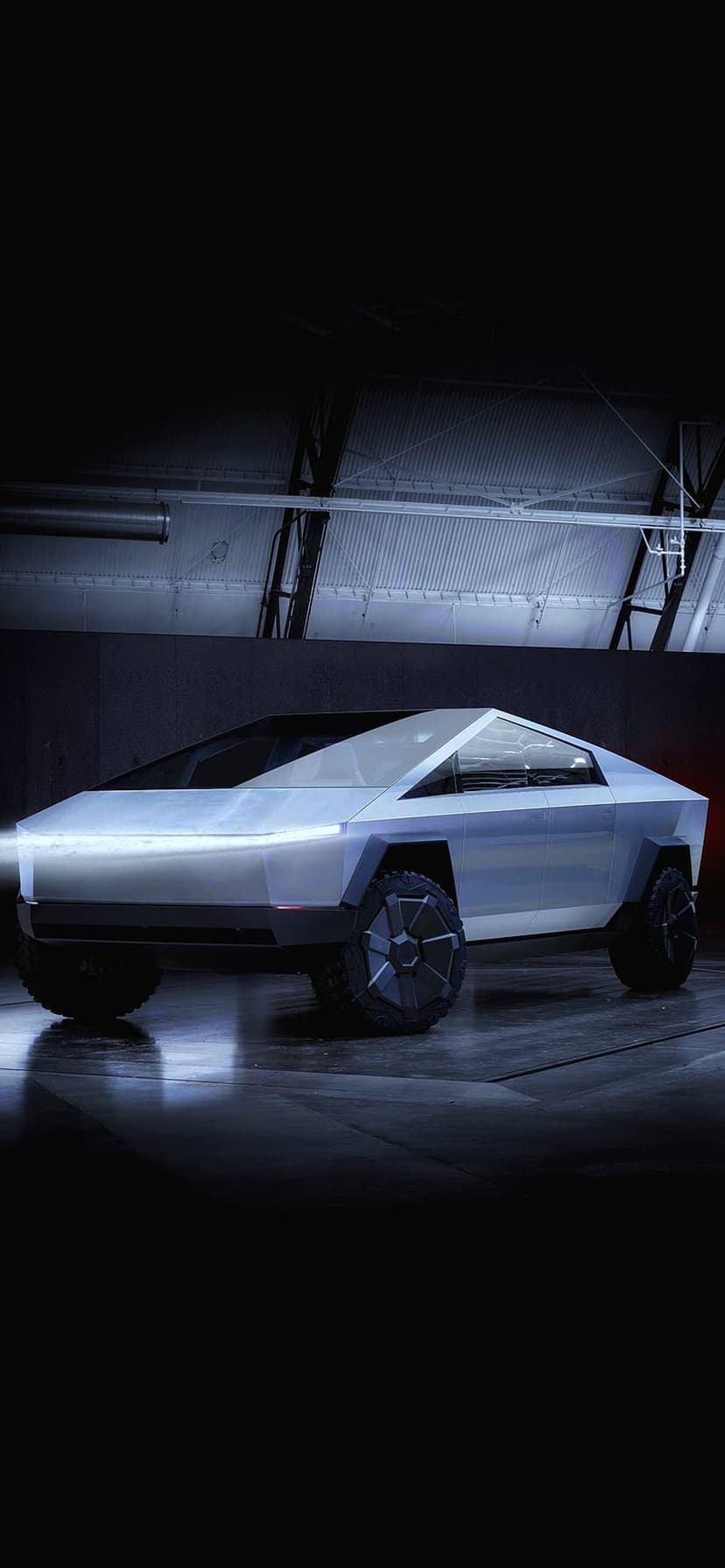 Tesla Cybertruck in a dark industrial garage with geometric steel panels and subtle overhead rim lighting.
