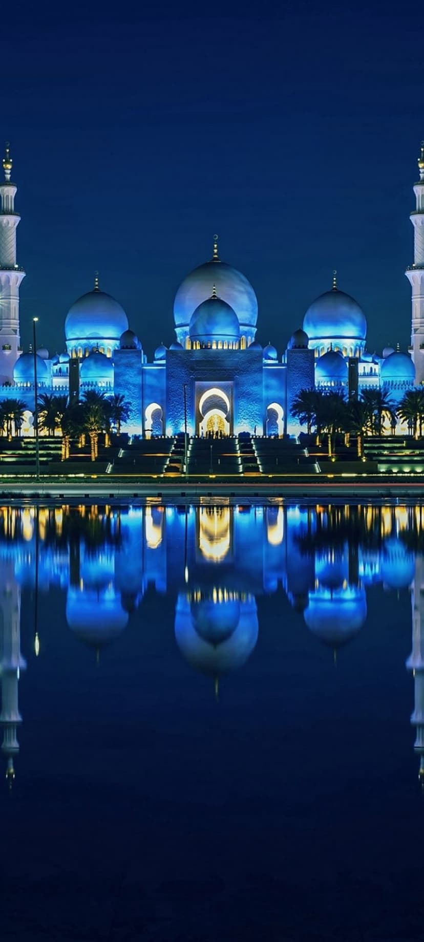 Sheikh Zayed Grand Mosque domes and minarets glow blue, reflecting in a calm pool under a dark night sky.