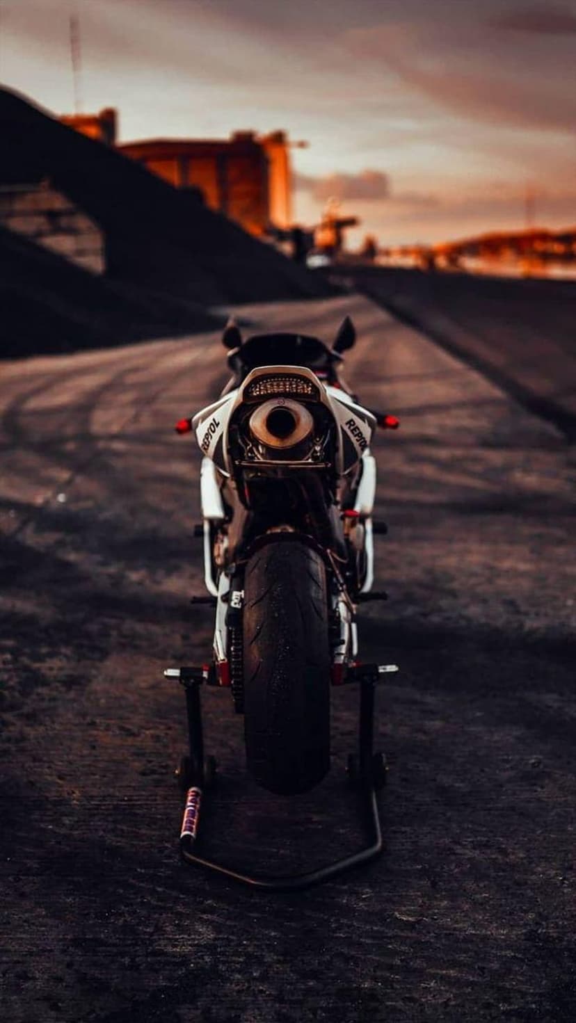 White and red sport motorcycle rear view on an asphalt road with a glowing orange sunset and exhaust detail.