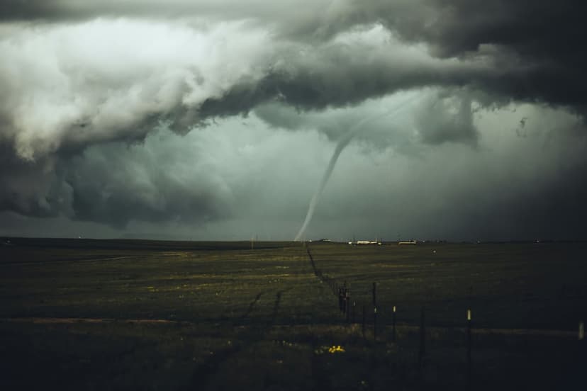 Tornado funnel cloud touching down in a flat rural field under a dark, heavy sky with a dirt road in the foreground.