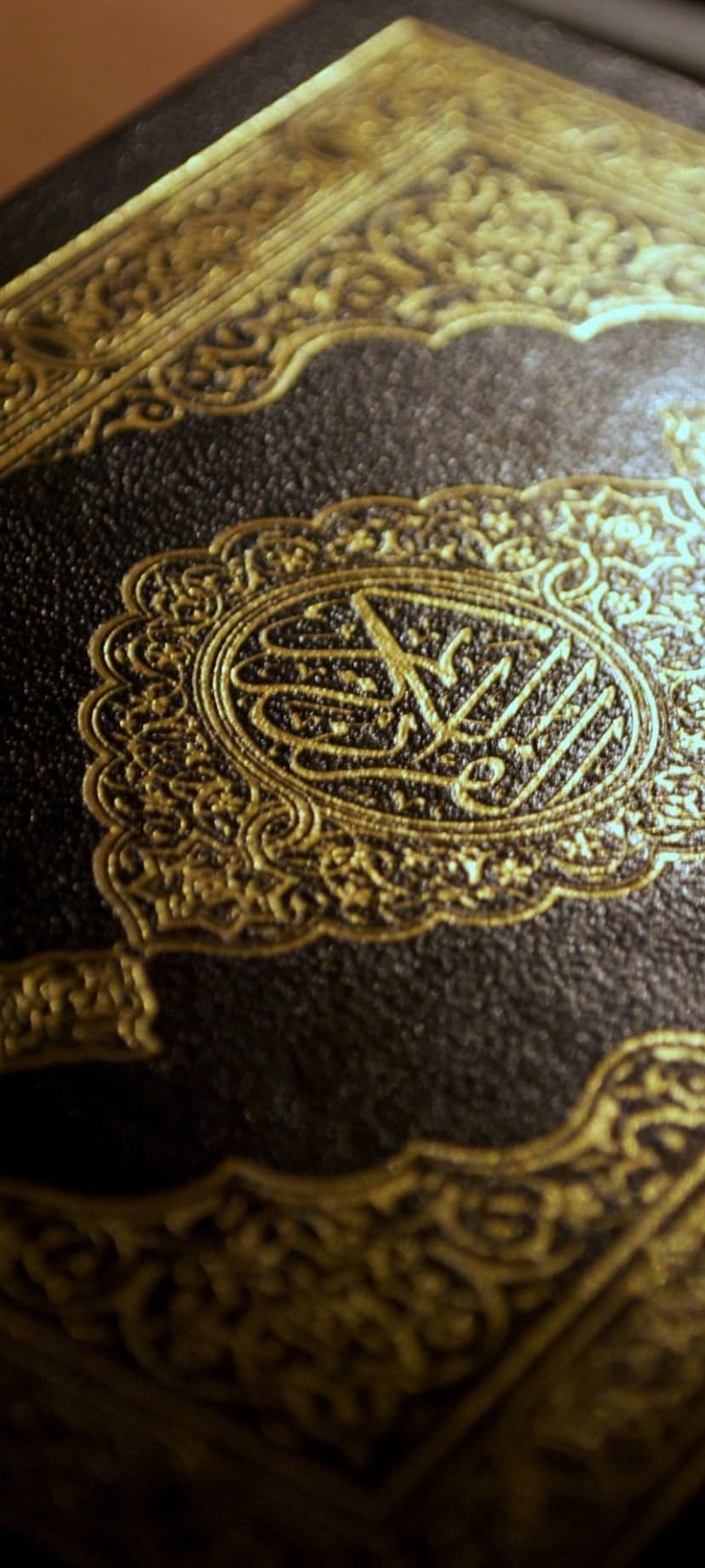 Gold Arabic script within an ornate oval frame on a dark textured cover with intricate Islamic geometric patterns.