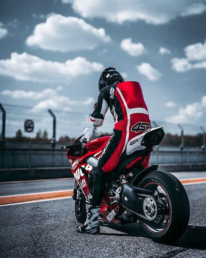 Motorcyclist wearing red and white leathers with number 45 leans a red racing bike on a blurred asphalt track.