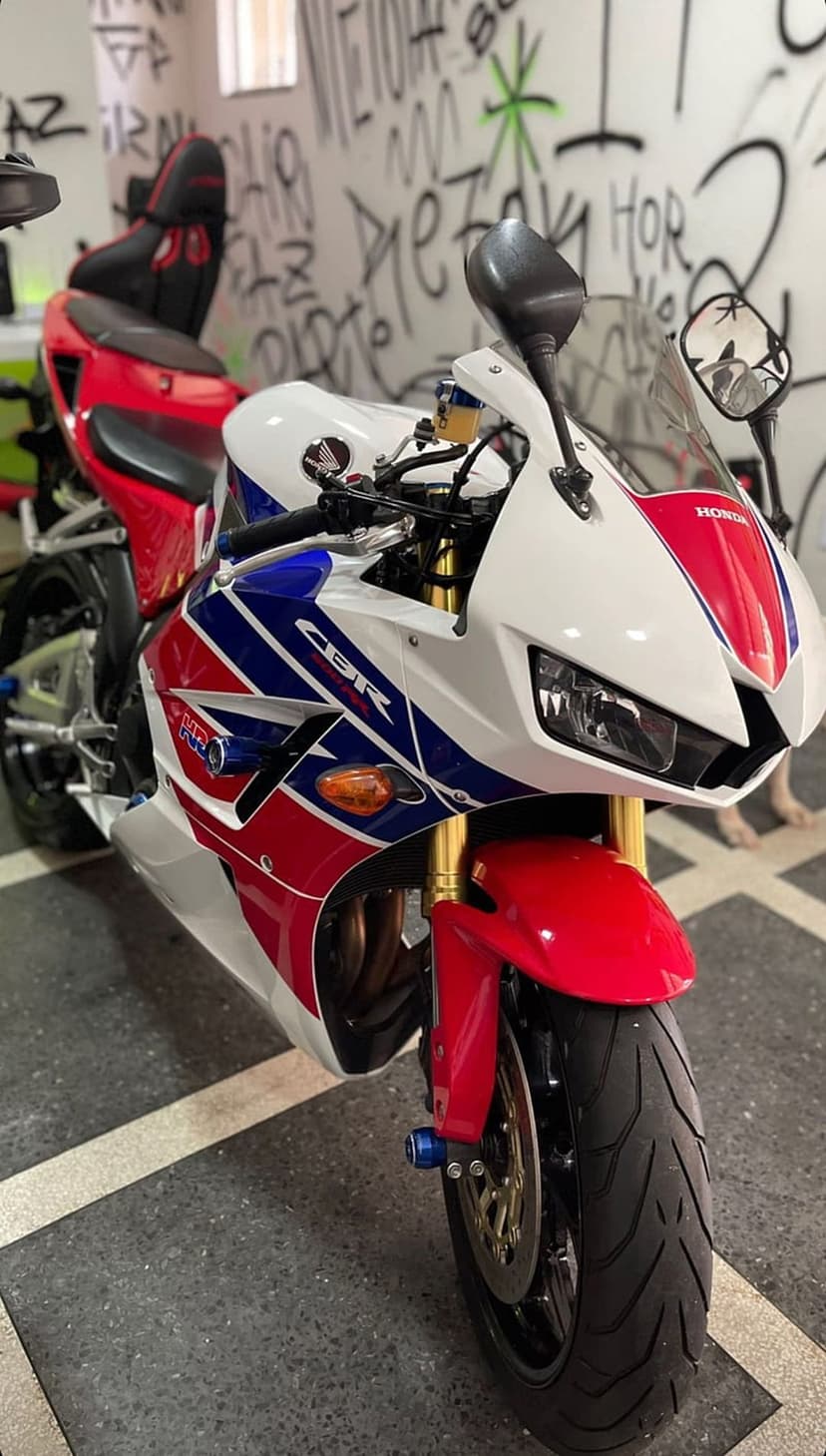 Honda CBR sportbike in tricolor livery stands before a graffiti wall with gold suspension and black tires.